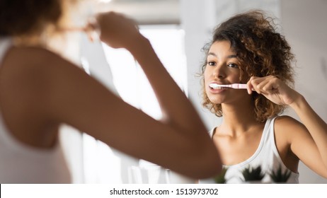 African American Girl Brushing Teeth With Toothbrush Looking In Mirror In Bathroom. Dental Care Concept. Panorama, Selective Focus