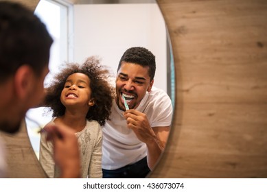 African american girl brushing teeth with dad.