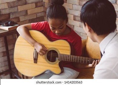 African American girl in casual outfit learning how to play guitar while sitting on couch near male tutor during music lesson - Powered by Shutterstock