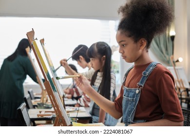 African American girl concentrates on acrylic color picture painting on canvas with students group in art classroom, creative learning with talents and skills in elementary school studio education. - Powered by Shutterstock