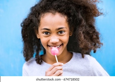 African American Girl With Curly Hair Outdoors Eating Lollipop.