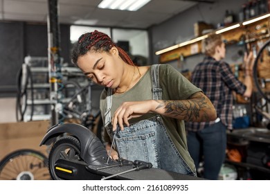 African american girl cycling repairman fixing electric scooter with screwdriver with her blurred female colleague on background in modern workshop. Bike service, repair and upgrade - Powered by Shutterstock