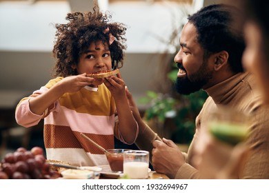 African American Girl Having Breakfast With Her Parents And Eating Toasted Bread With Jam At Dining Table. 