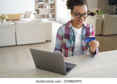 African American Girl Holding Banking Credit Card, Shopping Purchasing Online, Using Laptop, Making Payment. Smiling Teen Paying Using E-bank Service, Sitting At Desk At Home. E-commerce.