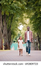 African American Girl Holding Hands With Grandfather And Walking In Park 