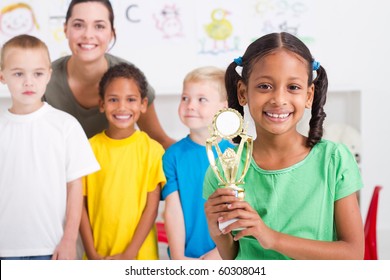 African American Girl Holding A Trophy In Front Of Classmates