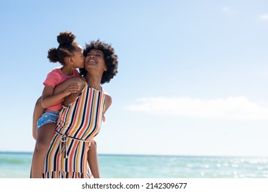 African american girl kissing mother while enjoying piggyback ride on her at beach against blue sky. unaltered, family, lifestyle, togetherness, enjoyment and holiday concept. - Powered by Shutterstock