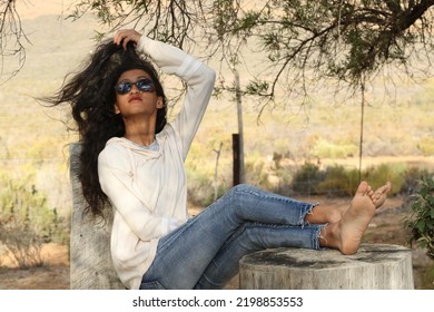 African American Girl With Long Wavy Hair Resting On Tree Stumps. Olive Skin Tone. Scenic Natural Background 