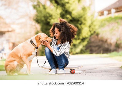 African American Girl Outdoors On Skateboard With Her Dog.