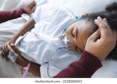 African american girl patient lying on bed with oxygen mask, with her mother at hospital. Hospital, motherhood, family, medicine and healthcare, unaltered. - Powered by Shutterstock