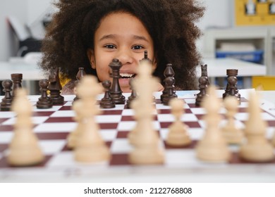 African American Girl Playing Chess. Happy Smiling Child Behind Chess Smiling In Class Or School Lesson. Excited Clever Black Kid With Board Game Close-up