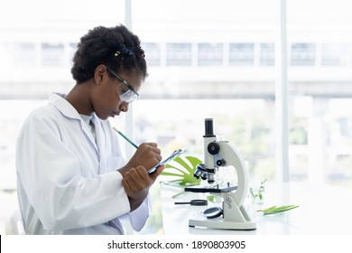 African American girl scientists learning and writing science and doing analysis for germs and bacteria with microscope in the laboratory. Science and education, researcher and discovery concept