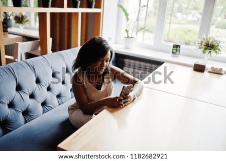 African american girl sitting at cafe with mobile phone at hand.