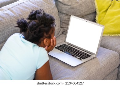 African American Girl Watching Laptop With Blank Screen While Lying On Sofa At Home, Copy Space. Unaltered, Domestic Life, Wireless Technology, Digital Native And Childhood Concept.