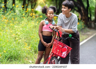 African American Girl Wearing Workout Clothes Happy Listening To Music On Headphones
With Asian Mothers Cycling In The Garden Together In The Park. Family Relax Concept.