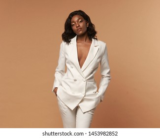 African american girl in white suit with wavy hair and make-up posing on a beige background. Fashion style full length studio portrait. Elegant fashionable woman