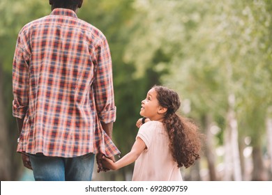 African American Granddaughter Holding Hands With Grandfather And Walking In Park 