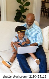 African american grandfather and his granddaughter using laptop together sitting on couch at home. family, love and technology concept, unaltered.