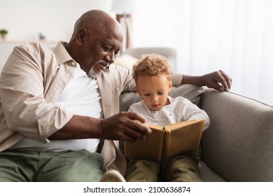 African American Grandpa And Grandson Reading A Book Spending Time Together Sitting On Couch At Home On Weekend. Senior Grandfather Teaching Grandchild To Read Indoors. Knowledge, Family Leisure - Powered by Shutterstock