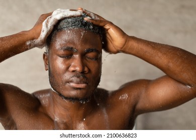 African American Guy Applying Shampoo On Hair Washing Head Touchind And Massaging It With Hands Standing Closing Eyes Taking Shower Indoor. Male Beauty Routine And Cosmetics Concept.