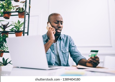 African American Guy In Casual Outfit Talking On Phone And Reading Credit Card Number While Sitting At Cafe Table And Working