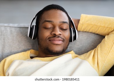 African American Guy With Closed Eyes Relaxing On Couch, Using Brand New Wireless Headset, Listening To Music, Closeup Portrait. Joyful Young Black Man Listening To Audiobook At Home