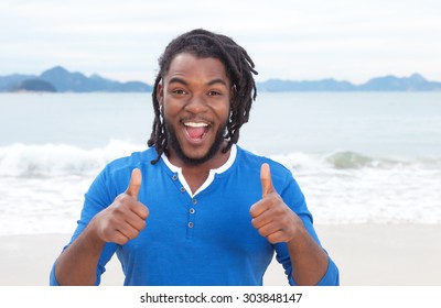 African american guy with dreadlocks at beach showing both thumbs