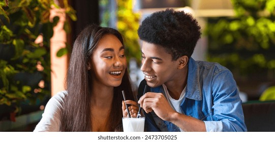 African American guy and girl are seated at a table, enjoying milkshakes. They are engaged in conversation while sipping on their drinks, have date - Powered by Shutterstock