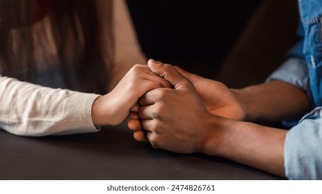 African American guy and girl are seated at a table, holding hands. They appear to be engaged in a conversation, with their hands intertwined in a gesture of closeness and connection, cropped - Powered by Shutterstock