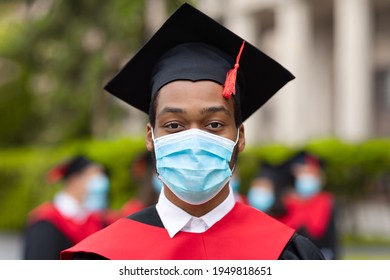 African American Guy In Graduation Costume And Protective Face Mask, Black Man Student Posing Over International Group Of Students At University Campus, 2021 Graduation Concept