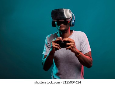 Hombre afroamericano jugando videojuegos con auriculares de mando y vr, disfrutando del juego online con simulación 3d futurista en estudio. Jugador con gafas de realidad virtual con joystick.