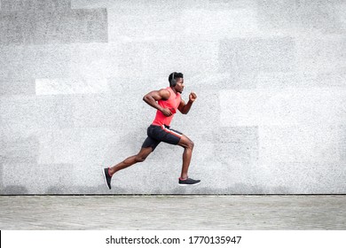 African American guy runner runs fast forward against the background of the city wall, sports man train on the street, general plan - Powered by Shutterstock