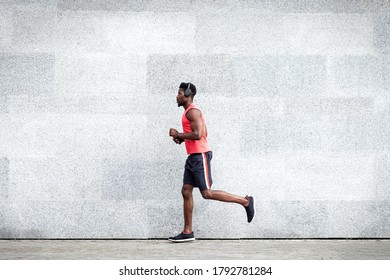African American guy runner runs fast forward against the background of the city wall, sports man train on the street, general plan