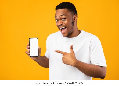 African American Guy Showing Smartphone Empty Screen Recommending Mobile Application Smiling To Camera Over Yellow Studio Background. Mockup