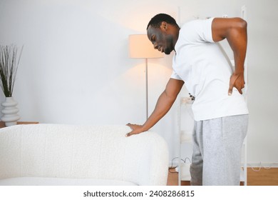 African American guy suffering from back pain, leaning on sofa, cannot walk at home. - Powered by Shutterstock