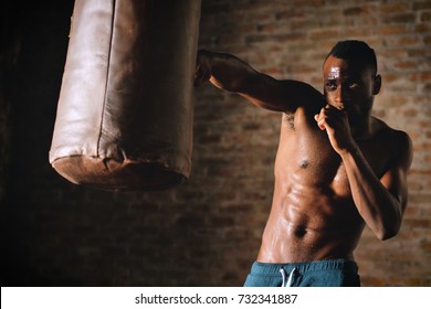 An African American guy trains in a vintage gym and fists his boxing bag fists. Concept of: gym, fitness, boxing, success, workout and power