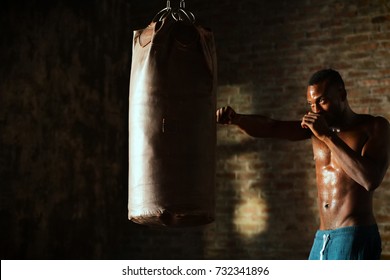 An African American guy trains in a vintage gym and fists his boxing bag fists. Concept of: gym, fitness, boxing, success, workout and power - Powered by Shutterstock