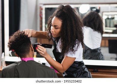 African american hairdresser in apron trimming head of client in salon