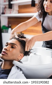 African American Hairdresser Washing Hair Of Young Man Near Sink