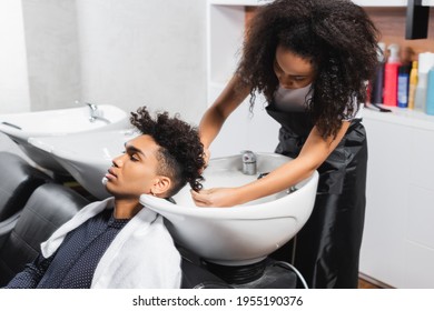 African american hairstylist washing hair of man in towel