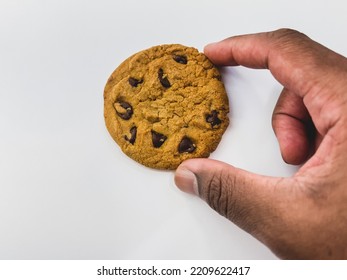 African American Man’s Hand Holding A Chocolate Chip Cookie Against White Background