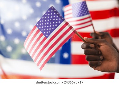 African American hand holding an American flag with another flag in the background. The focus on the flag symbolizes patriotism and national pride. - Powered by Shutterstock