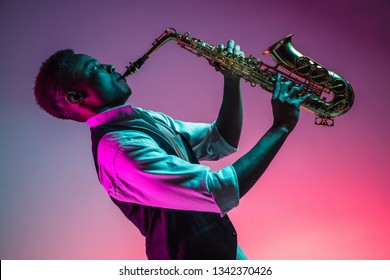 African American handsome jazz musician playing the saxophone in the studio on a neon background. Music concept. Young joyful attractive guy improvising. Close-up retro portrait.