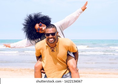 African American Happy Couple Having Fun Piggyback Riding And Playing Airplane On The Beach - Black Man And Afro Hair Woman In Playful Moment On The Shore At Summer Time - Concept Of Happiness Image