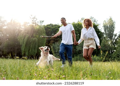 african american happy couple walk and run together with dog in park in summer, man and woman actively play with golden retriever and throw stick to him in nature, freedom and pets concept - Powered by Shutterstock