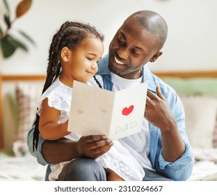 African american happy family father with baby daughter hugging smiling  while celebrating Fathers day together at home. Little girl congratulating giving dad homemade greeting postcard - Powered by Shutterstock