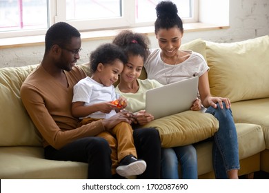 African American Happy Family With Two Children Having Good Time Using Laptop. Young Diverse Smiling Husband And Wife With Cute Daughter And Son Sitting On Couch At Home Looking At Computer.