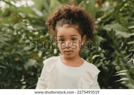 African American happy little girl, against the background of decorative leaves in the garden.