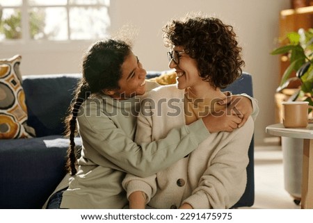 African American happy teenage girl embracing her foster mom while they spending time together at home