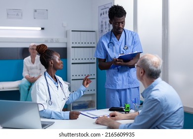 African American Healthcare Hospital Staff Reviewing Senior Patient Record File While Talking About Treatment Schedule. Clinic Expert Discussing With Nurse About Consultation Appointments